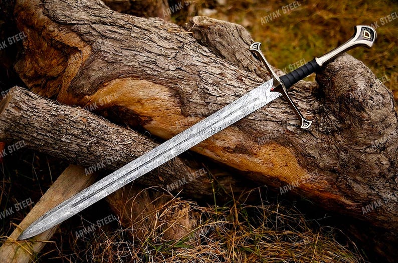 May include: A long, silver sword with a patterned blade rests on a weathered log. The sword features a black handle and a silver crossguard and pommel. The blade has a detailed, textured design. The sword is a fantasy or historical item.