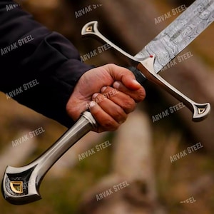 May include: A detailed image of a sword with a patterned blade and ornate silver hilt. The hilt features a gold accent. The sword is held in a hand, with the text "ARVAK STEEL" visible in the background.