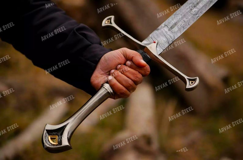 May include: A detailed image of a sword with a patterned blade and ornate silver hilt. The hilt features a gold accent. The sword is held in a hand, with the text "ARVAK STEEL" visible in the background.