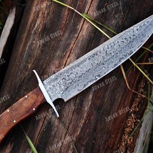 May include: A large, ornate knife with a patterned steel blade and a wooden handle. The blade has a unique, swirling design. The handle is dark brown with brass rivets. The knife is labeled "ARVAK STEEL".