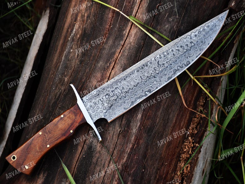 May include: A large, ornate knife with a patterned steel blade and a wooden handle. The blade has a unique, swirling design. The handle is dark brown with brass rivets. The knife is labeled "ARVAK STEEL".