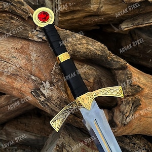 Può includere: Una spada in stile medievale con una lama argentata e una guardia dorata. L'impugnatura è avvolta in materiale nero con dettagli dorati. Il pomo presenta una gemma rossa. Il testo "ARVAK STEEL" è visibile.