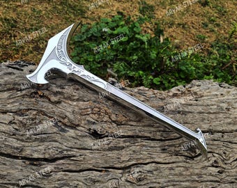 Puede incluir: Un hacha plateada con una hoja curva y grabados decorativos. La cabeza del hacha tiene forma de media luna con diseños intrincados. El mango es largo y recto, con un extremo puntiagudo. El hacha se exhibe sobre una superficie de madera envejecida.