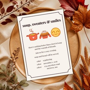 May include: A rectangular invitation card with a black border featuring the text soup, sweaters & smiles, icons of a red soup pot, a striped sweater, and a yellow smiley face, plus event details for a gathering on november 1, 2026, at 1234 anywhere road.