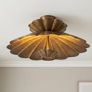 May include: A flush mount ceiling light fixture with a tiered, scalloped shell design in an antique brass finish. The fixture features a wide, fluted shade and a smaller, matching scalloped element suspended from a central rod, emitting a warm glow.