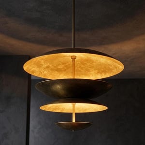 May include: A multi-tiered pendant light fixture featuring four stacked, bowl-shaped discs of varying sizes. The interior surfaces of the discs have a textured, metallic gold finish that glows when illuminated, while the exterior is a dark bronze.