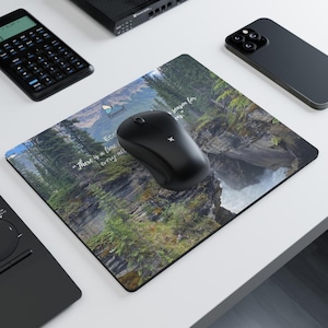 May include: A rectangular mousepad featuring a scenic landscape with a waterfall and forest. The mousepad has the text "There is a time for every act" and "Eco Renewal". A black wireless mouse sits on the pad.