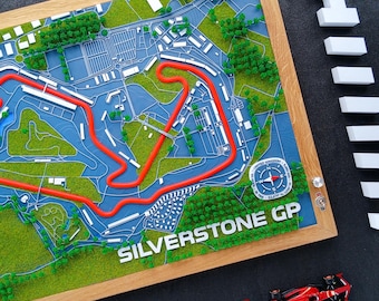 Könnte beinhalten: Ein gerahmter 3D-Plan der Silverstone GP-Rennstrecke mit roter Streckenführung auf einer blau-grünen Landschaft. Die Worte "SILVERSTONE GP" sind zu sehen. Ein kleines rotes Modellrennauto befindet sich darunter.