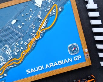 Könnte beinhalten: Eine gerahmte 3D-Karte des Saudi-Arabien Grand Prix-Rennkurses mit einem leuchtend blauen Hintergrund und einer gelben Strecke. Die Karte ist in einem Holzrahmen eingefasst. Die Worte "SAUD ARABIAN GP" sind zu sehen. Ein Spielzeug-Rennwagen ist ebenfalls sichtbar.