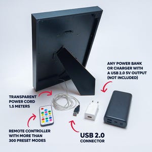 Back view of an LED neon wall art frame showing the stand and transparent 1.5-meter power cord. Includes a USB 2.0 connector, a remote controller with over 300 lighting modes, and examples of compatible power sources such as a USB wall charger and power bank (not included).