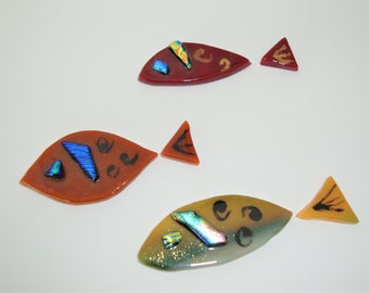 May include: Three glass fish mosaic pieces with iridescent accents. The fish are in shades of red, orange, and yellow. The pieces are separated and ready to be assembled.