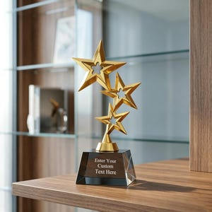 May include: A gold-colored trophy featuring three stacked star shapes with cut-out centers, mounted on a black, trapezoidal base. The front of the base displays the white text, Enter Your Custom Text Here, in a clear, sans-serif font style.