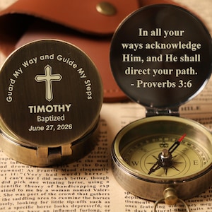 May include: A brass compass with a hinged lid, engraved with text and a cross symbol. The open compass shows a directional dial. The lid displays the text "In all your ways acknowledge Him, and He shall direct your path."