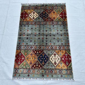 A hand-knotted small Afghan Gabbeh area rug from IMG_9772.jpg featuring a minimalist sage-grey center field adorned with tiny geometric accents, framed by thick top and bottom panels filled with vibrant, colorful diamond medallions in red, navy, green, and gold.