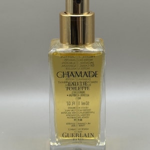Könnte beinhalten: Eine klare Glasflasche von Guerlain Chamade Eau de Toilette. Die Flasche hat einen goldfarbenen Verschluss und eine rechteckige Form. Das Etikett zeigt den Markennamen und Produktdetails in vertikaler Anordnung. Die Flüssigkeit im Inneren ist hellgelb.