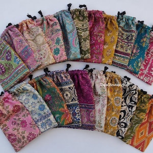 Può includere: Una collezione di sacchetti rettangolari in tessuto con coulisse, disposti a semicerchio. Ogni sacchetto presenta un motivo unico e colorato con disegni floreali, geometrici o paisley in varie tonalità di rosa, verde, blu, giallo e oro.
