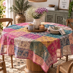 May include: A round tablecloth featuring a vibrant patchwork design with various floral and geometric patterns in shades of pink, yellow, teal, and blue. The fabric drapes over a circular table, creating a colorful display for the dining area.