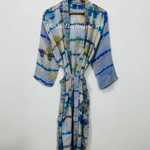 May include: A long, flowing robe with a tie belt, featuring a blue and white tie-dye pattern. The robe is hanging on a wooden hanger. The text "Royal Heritage Craft" is visible on the robe.