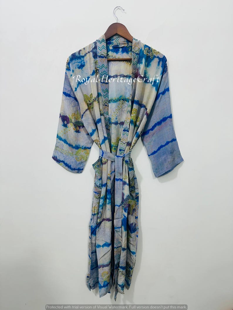 May include: A long, flowing robe with a tie belt, featuring a blue and white tie-dye pattern. The robe is hanging on a wooden hanger. The text "Royal Heritage Craft" is visible on the robe.