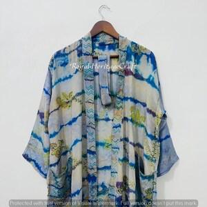 May include: A tie-dye kimono in shades of blue, white, and purple, with floral embroidery and the text "Royal Heritage Craft". The kimono is hanging on a wooden hanger.