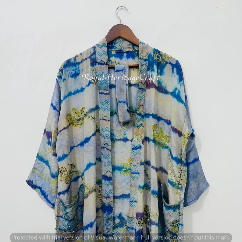 May include: A tie-dye kimono in shades of blue, white, and purple, with floral embroidery and the text "Royal Heritage Craft". The kimono is hanging on a wooden hanger.