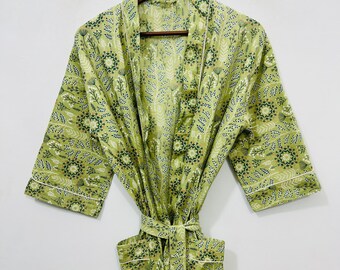 May include: A light green robe with a floral pattern in dark green and white. The robe has a matching belt, pockets, and white trim along the edges. It is hanging on a wooden hanger.