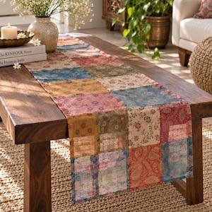 May include: A rectangular table runner featuring a patchwork design of various floral and paisley patterns in shades of blue, red, yellow, and green. The fabric displays a grid of distinct squares, each with a unique print, creating a colorful textile.