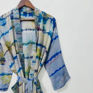 May include: A tie-dye patterned robe in shades of blue, white, and gold hangs on a wooden hanger. The robe features a belt and the text "Royal Heritage Craft". The sleeves have a striped design.