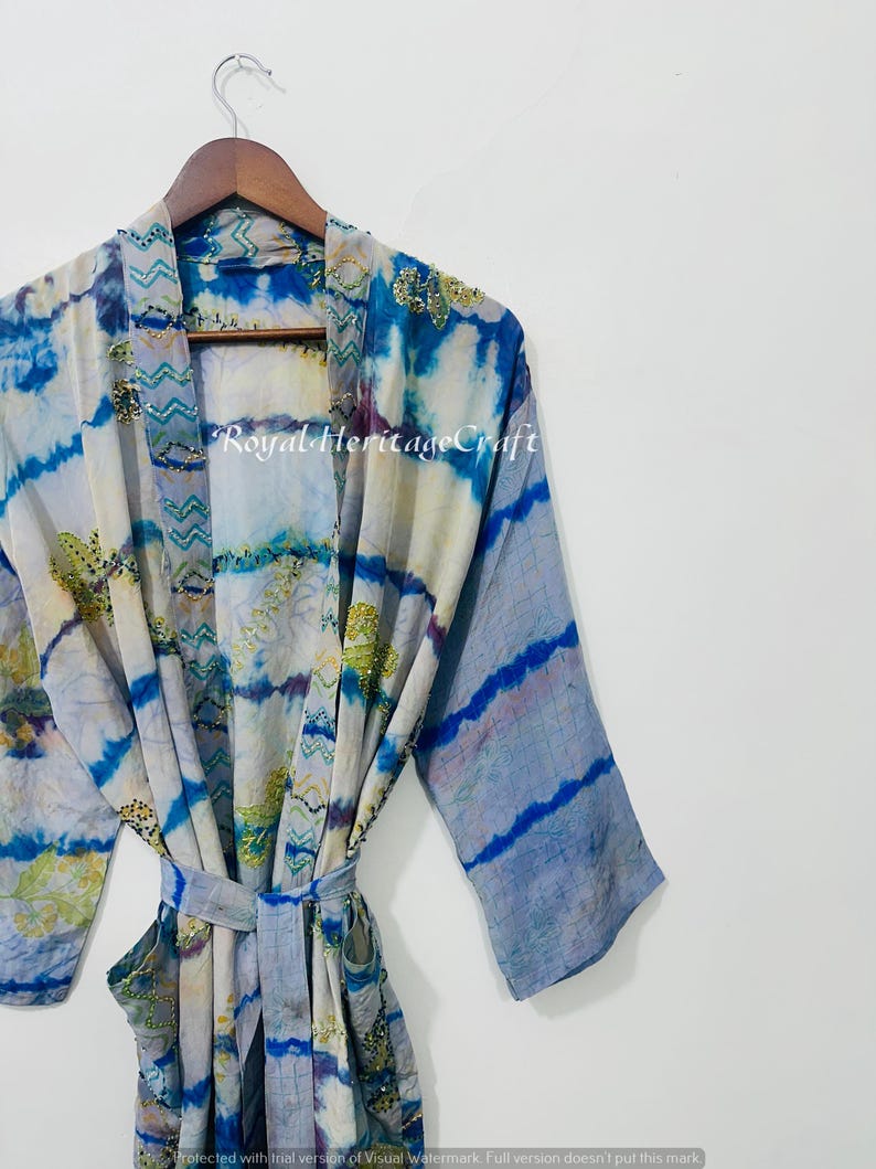 May include: A tie-dye patterned robe in shades of blue, white, and gold hangs on a wooden hanger. The robe features a belt and the text "Royal Heritage Craft". The sleeves have a striped design.