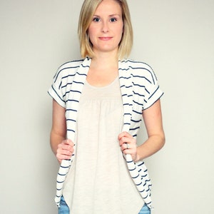 May include: A woman wearing a white and navy striped cardigan over a beige t-shirt and blue jeans.