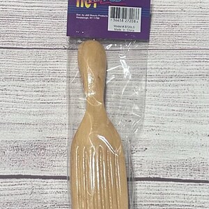 Puede incluir: Una herramienta de peinado de madera con un mango y una cabeza ancha y acanalada, empaquetada en una bolsa de pl&aacute;stico transparente. El embalaje incluye el texto "HOT WAVES" e informaci&oacute;n del producto. La herramienta est&aacute; fabricada en China.