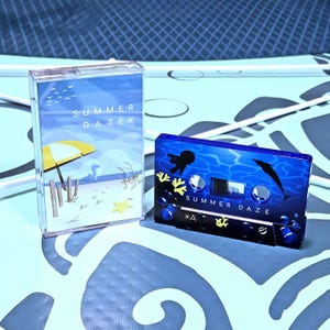 May include: Two cassette tapes with "Summer Daze" printed on them. One tape is in a clear case with a beach scene, yellow umbrella, and blue sky. The other tape is blue with a dolphin and jellyfish design.