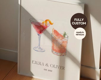 May include: A framed print featuring watercolor illustrations of two cocktails: a martini with an orange peel and a drink with a grapefruit slice. The print includes the names "Emma & Oliver" and "EST. 2022". A circular sticker says "FULLY CUSTOM" and "ready in 48 hours".