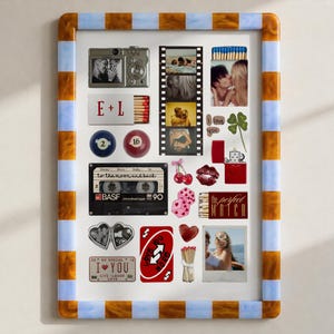 May include: A rectangular wall art print in a blue and amber striped frame featuring a collage of romantic items including a camera, film strip, cassette tape, matchboxes with text E+L and The Perfect Match, playing cards, and various heart motifs.