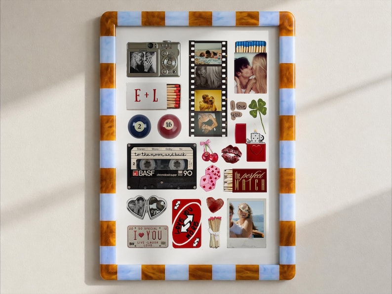 May include: A rectangular wall art print in a blue and amber striped frame featuring a collage of romantic items including a camera, film strip, cassette tape, matchboxes with text E+L and The Perfect Match, playing cards, and various heart motifs.