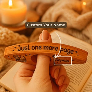 May include: A wooden book page holder with the text "Just one more page" and a cat illustration. The holder is personalized with the name "Sophia". The holder is designed to be held with a finger.