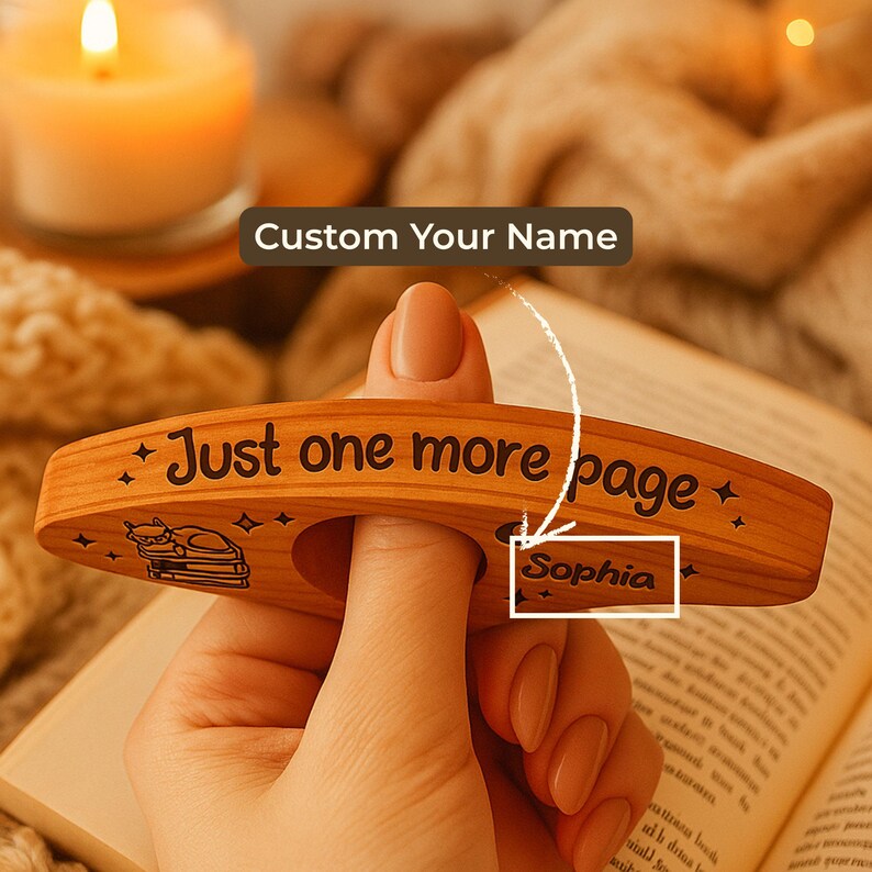 May include: A wooden book page holder with the text "Just one more page" and a cat illustration. The holder is personalized with the name "Sophia". The holder is designed to be held with a finger.