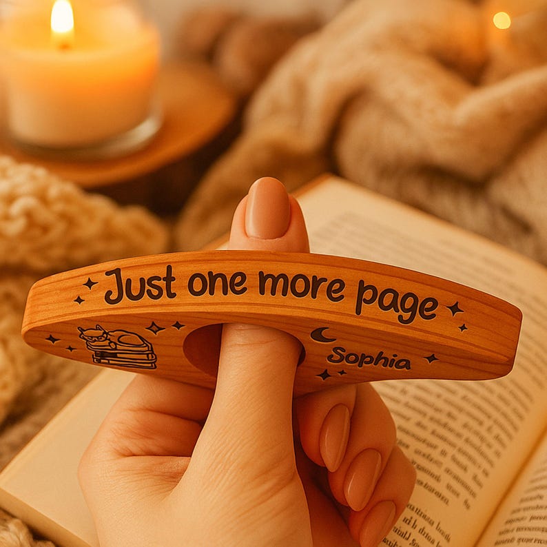 May include: A wooden thumb page holder with the text "Just one more page" and the name "Sophia". The page holder has a cat and book design and is held over an open book.