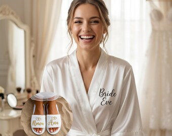 May include: A smiling person wearing a white satin robe with the words "Bride Eve" in black script. The image also shows white slippers with gold text that reads "Nowa Ana". The robe has a tie closure.