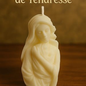 Könnte beinhalten: Elfenbeinfarbene Kerze in Form einer Frau mit langem, fließendem Haar und drapierter Kleidung. Die Kerze hat einen Docht und trägt die Aufschrift "Notre-Dame de Tendresse".