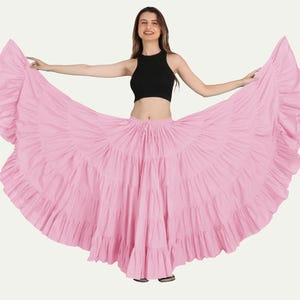May include: A light pink, tiered skirt with a ruffled hem. The skirt is full and flowing, with a drawstring waist. The model is wearing a black crop top.