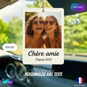 May include: A rectangular car air freshener with a photo of two smiling women wearing sunglasses. The text "Chère amie Depuis 2012" is below the photo. The bottom of the air freshener reads "Désodorisant PERSONNALISE AVEC TEXTE".