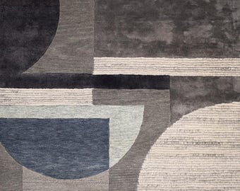 May include: Geometric patterned rug in shades of grey, blue, and white. The design features semi-circles, rectangles, and other shapes. The rug has a textured appearance, adding depth and visual interest to the design.