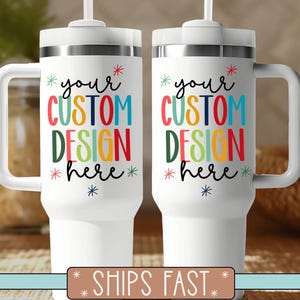 May include: Two white insulated tumblers with handles and straws. Each tumbler has the text "your CUSTOM DESIGN here" in colourful letters. The tumblers are designed for personalisation.