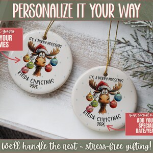 May include: Two round Christmas ornaments with a moose design. The ornaments have the text "It's a Merry-Moosemas Kinda Christmas 2025". Each ornament has a gold string for hanging. The ornaments are on a white tray.
