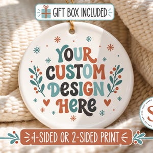 May include: A round white ceramic ornament featuring the text YOUR CUSTOM DESIGN HERE in multi-colored retro-style lettering. The design includes small snowflakes, red hearts, and green leafy sprigs with red berries. A gold string is attached at the top.