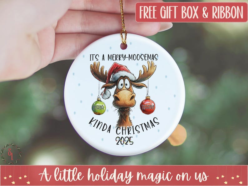May include: A white ceramic Christmas ornament featuring a cartoon moose wearing a Santa hat. The ornament has the text "IT'S A MERRY-MOOSEMAS KINDA CHRISTMAS 2025" and two hanging ornaments with the names "MAYA" and "REBECCA".