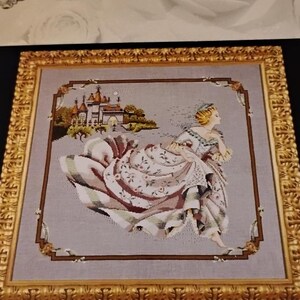 May include: Cross-stitch artwork featuring a woman in a flowing gown, set against a castle backdrop. The piece is framed in a gold ornate frame. The artwork is labeled "Mirabili cross-stitch" at the top.