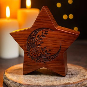 Puede incluir: Una estrella decorativa de madera con un diseño de luna creciente y flores talladas. El objeto es de color marrón cálido y está sobre una base de madera. Hay velas encendidas en el fondo.