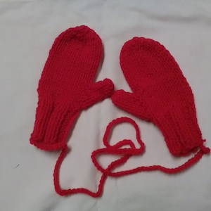May include: A pair of red knitted mittens with a matching red string tie. The mittens are made with a simple knit stitch and have a thumb hole.